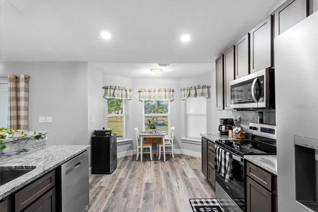 a kitchen with stainless steel appliances granite countertop a stove top oven a sink dishwasher a dining table and chairs with wooden floor