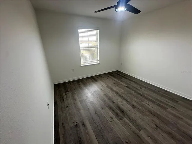 an empty room with wooden floor chandelier fan and windows