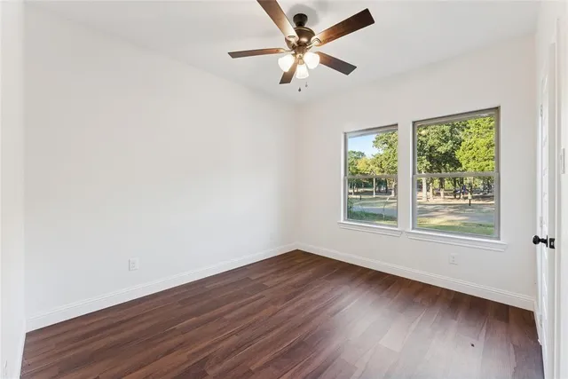 an empty room with wooden floor fan and windows
