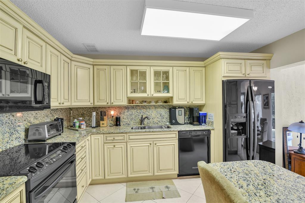 6693 Via Regina, Unit 6693 Boca Raton, FL 33433 - Photo 17 of 27 a kitchen with stainless steel appliances granite countertop a stove top oven a sink dishwasher a refrigerator and cabinets with wooden floor