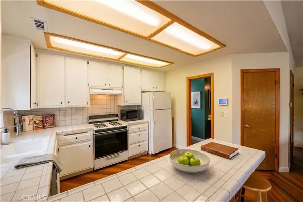 a kitchen with stainless steel appliances a stove a refrigerator a sink a dining table and chairs with wooden floor