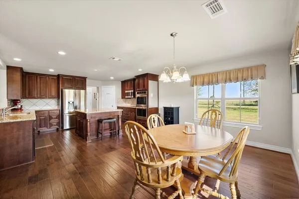 a kitchen with stainless steel appliances granite countertop a stove top oven a sink a refrigerator with a dining table and chairs with wooden floor