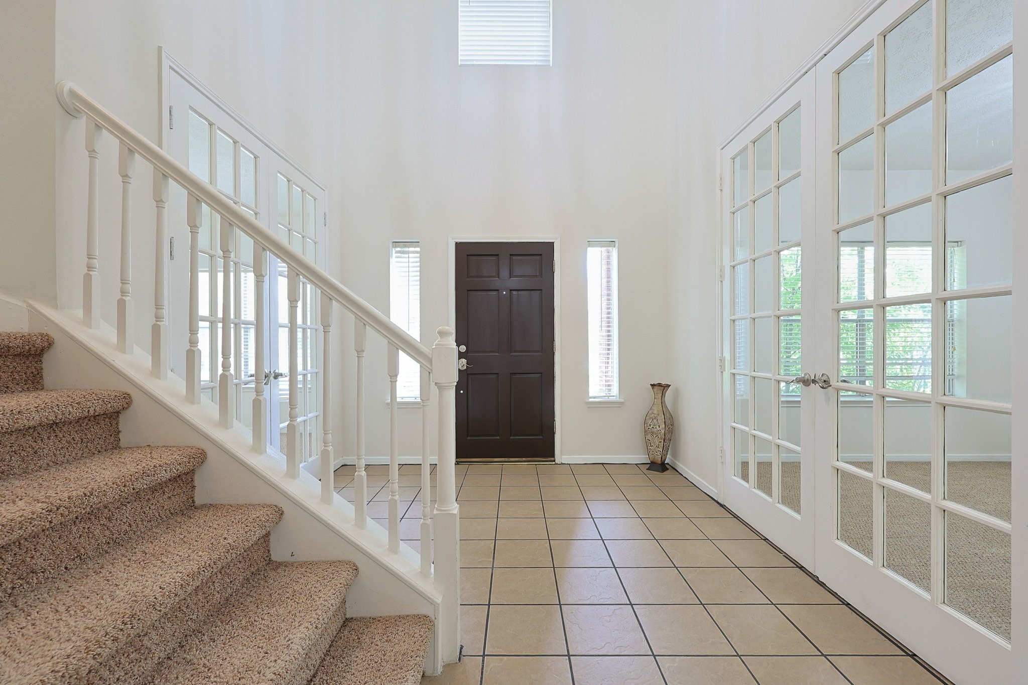 23019 Eastgate Village Drive Spring, TX 77373 - Photo 18 of 46 This is a bright and welcoming entryway featuring a tiled floor, a dark wood front door, and large windows. It includes a carpeted staircase with white railings and elegant French doors leading to another room.
