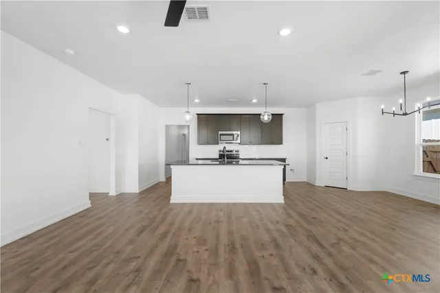 a large kitchen with kitchen island a stove a sink a refrigerator and white cabinets with wooden floor