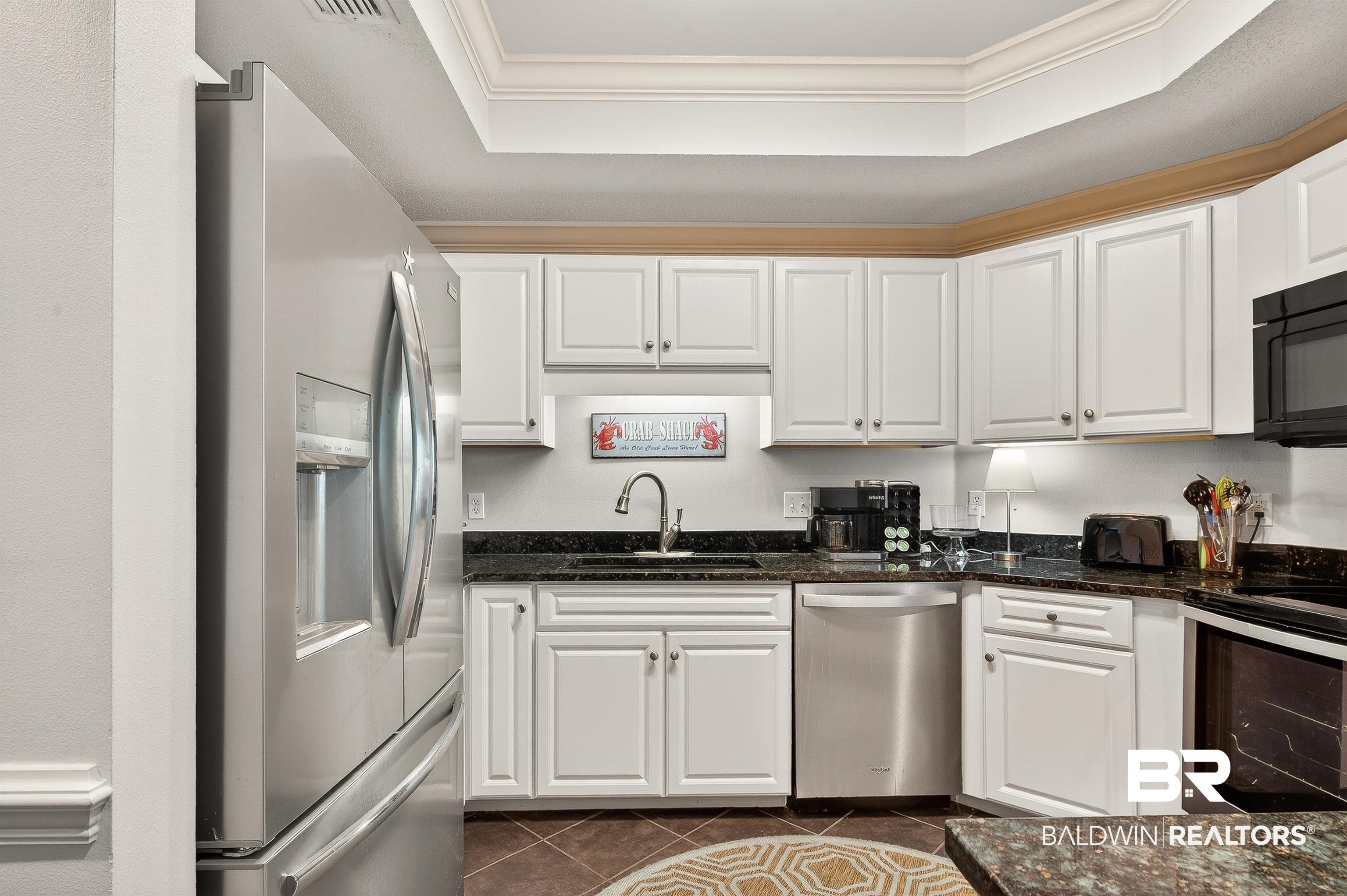 27582 Canal Road, Unit 2507 Orange Beach, AL 36561 - Photo 23 of 75 Kitchen with stainless steel appliances, white cabinets, a tray ceiling, crown molding, and dark stone countertops