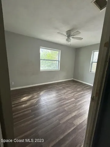 an empty room with wooden floor fan and windows