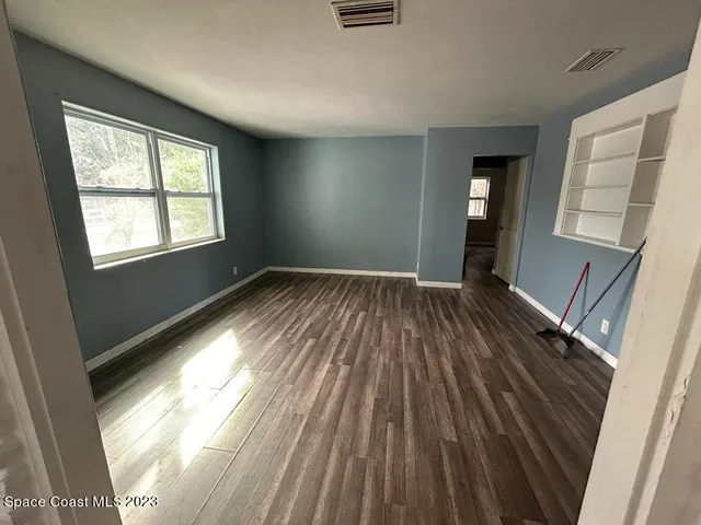 a view of an empty room with wooden floor and a window