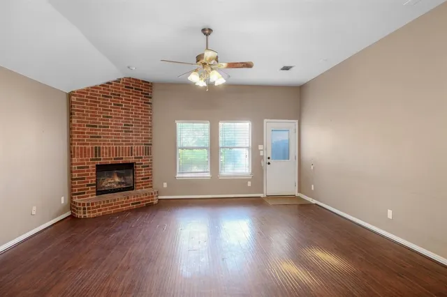 a view of an empty room with wooden floor fireplace and a window