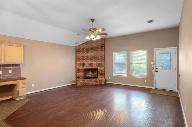 an empty room with wooden floor fireplace and windows