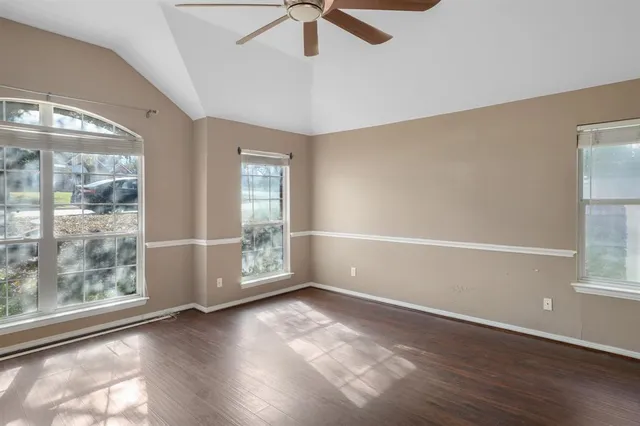 an empty room with wooden floor fan and windows