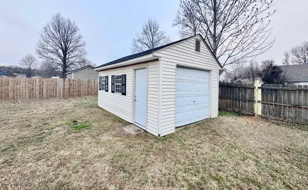 a view of a small white house with a large tree and wooden fence