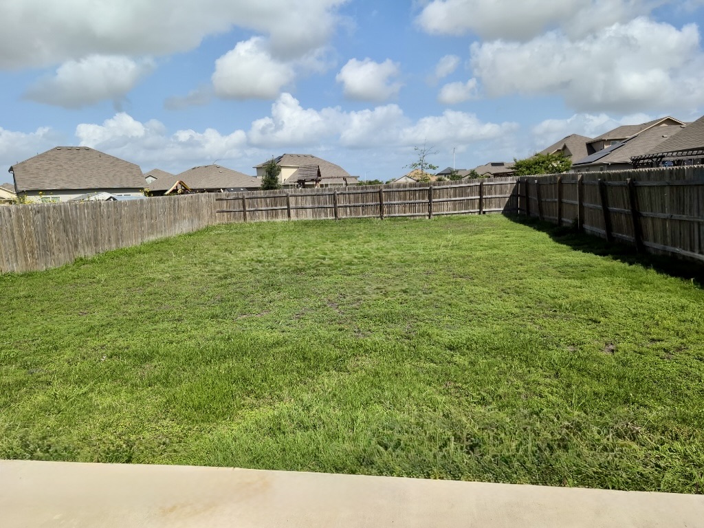 12040 Riparian Road Manor, TX 78653 - Photo 23 of 23 An expansive grassy lawn is fully enclosed by wooden privacy fencing under a blue sky.