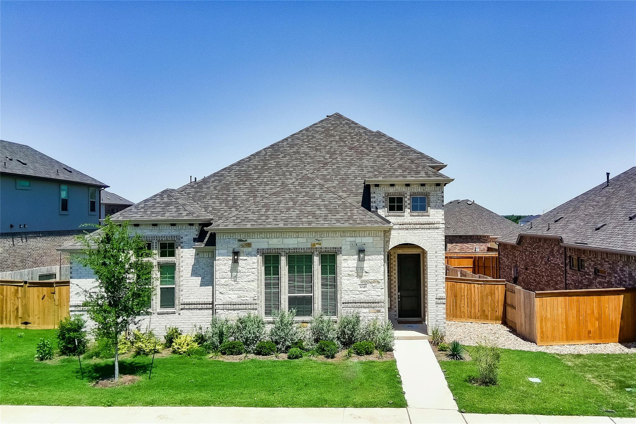 A well-maintained lawn and shrubbery complement the charming brick and stone facade of this residence.