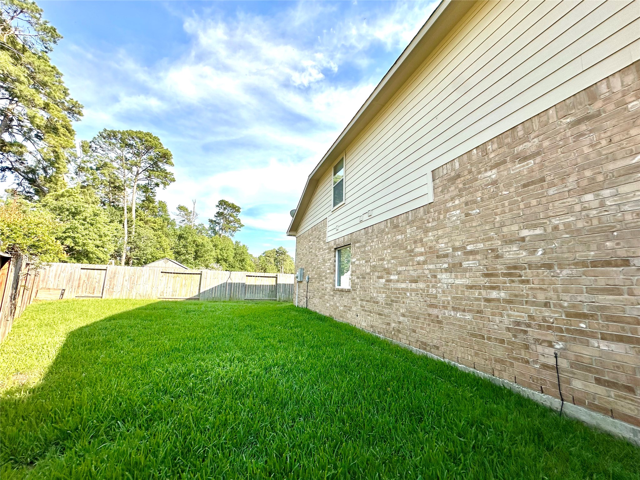 9611 Babbling Spring Court Tomball, TX 77375 - Photo 28 of 31 This photo shows a side view of a brick house with a spacious, well-maintained grassy backyard. It's enclosed by a wooden fence, offering privacy and a natural setting with trees in the background.
