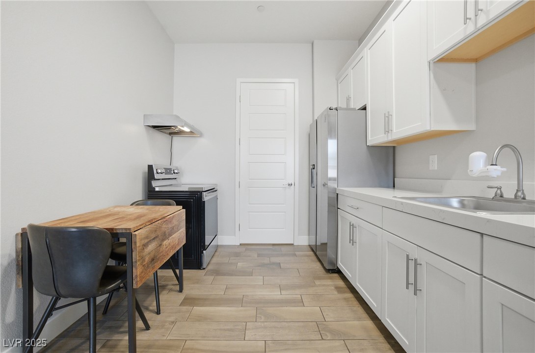 7736 Tioga Ridge Las Vegas, NV 89117 - Photo 48 of 68 Kitchen with stainless steel appliances, light countertops, white cabinets, wood finish floors, and wall chimney range hood