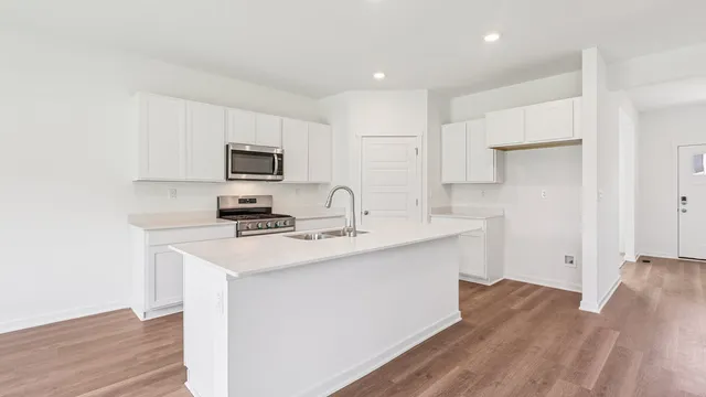 a kitchen with stainless steel appliances a stove top oven a sink a refrigerator white cabinets and wooden floor