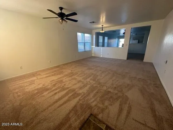 an empty room with chandelier fan and windows