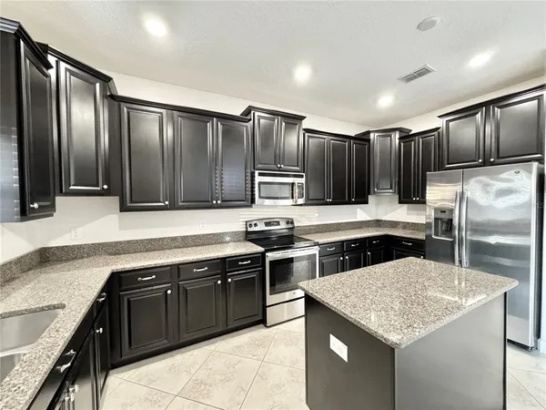 a kitchen with kitchen island granite countertop stainless steel appliances lots of counter top space cabinets a sink and a wooden floor