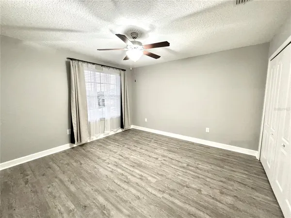 an empty room with wooden floor fan and windows