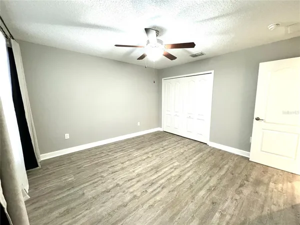 an empty room with wooden floor fan and windows