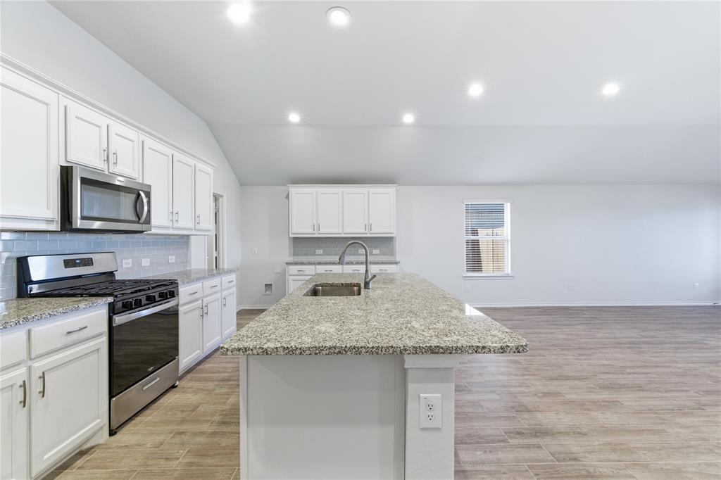 748 Ruellia Street Weatherford, TX 76086 - Photo 16 of 37 a kitchen with granite countertop a sink dishwasher stove and oven with wooden floor