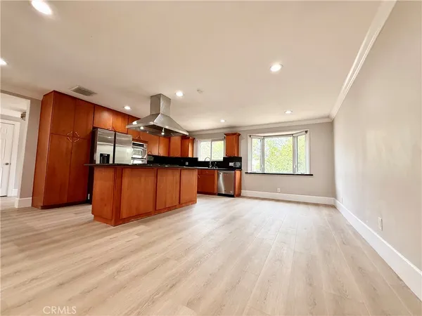 a view of an empty room with wooden floor and a kitchen
