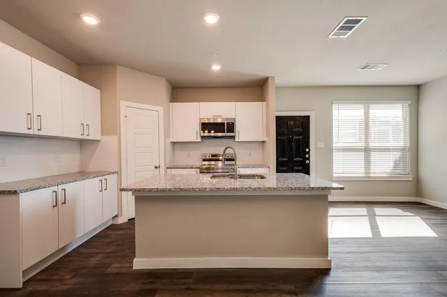 a large kitchen with stainless steel appliances granite countertop a stove a sink and a white wooden cabinets