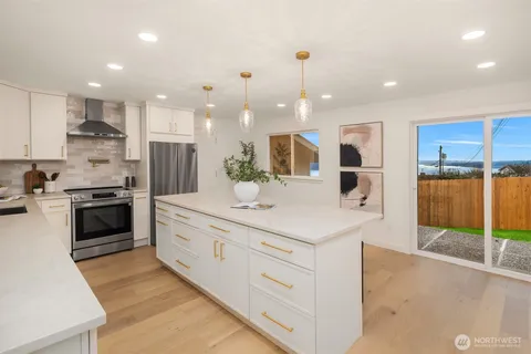 a large kitchen with stainless steel appliances kitchen island granite countertop a refrigerator a sink a stove and white cabinets with wooden floor