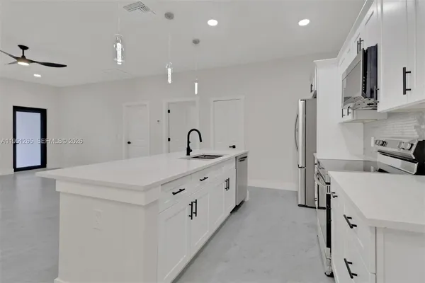 a large white kitchen with stainless steel appliances a sink window and cabinets