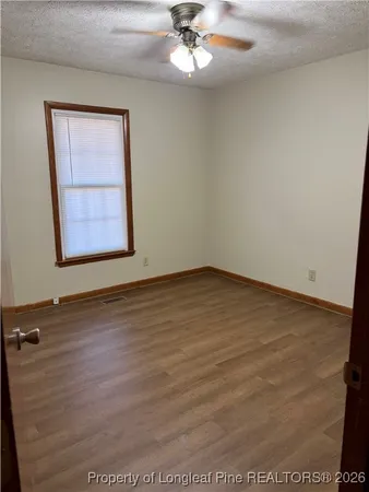 an empty room with wooden floor chandelier fan and windows