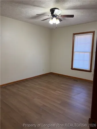an empty room with wooden floor chandelier fan and windows