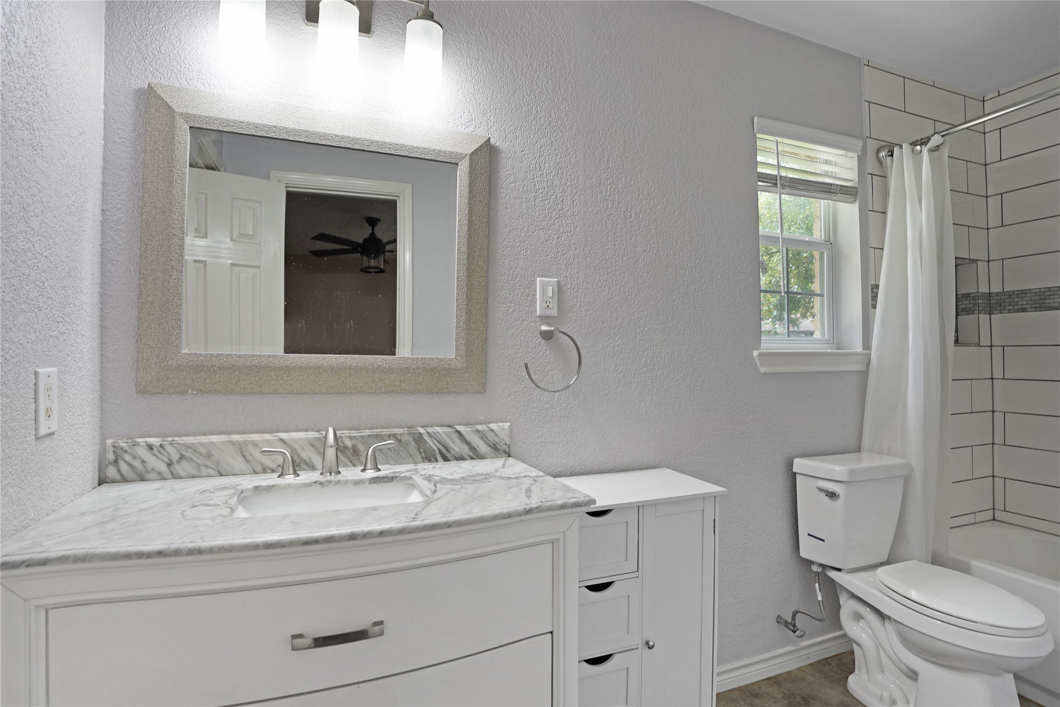 17119 Mellow Ridge Drive Spring, TX 77379 - Photo 19 of 32 This modern bathroom features a sleek marble countertop with an under-mount sink, a stylish mirror with overhead lighting, and a tiled shower area. The space is brightened by a window, offering a clean and contemporary feel.