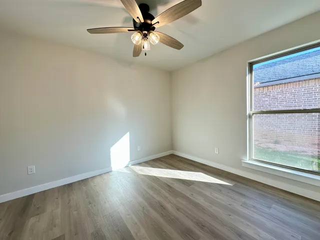 an empty room with wooden floor fan and windows