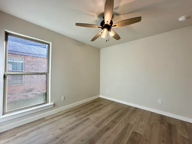 an empty room with wooden floor fan and windows