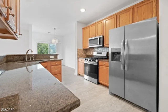 a kitchen with stainless steel appliances granite countertop a refrigerator a stove and a sink with wooden floor