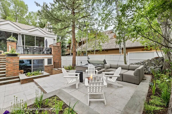 a view of a patio with couches table and chairs with wooden fence and large trees