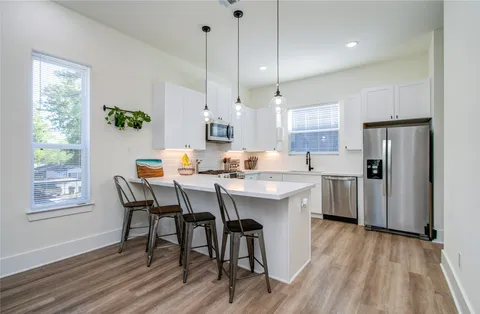 a kitchen with stainless steel appliances granite countertop a stove a refrigerator a kitchen island a sink dishwasher and white cabinets with wooden floor