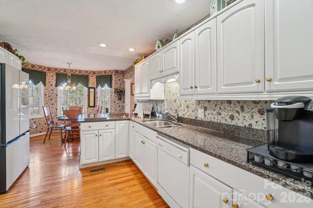 a kitchen with stainless steel appliances granite countertop a stove a sink and white cabinets with wooden floor