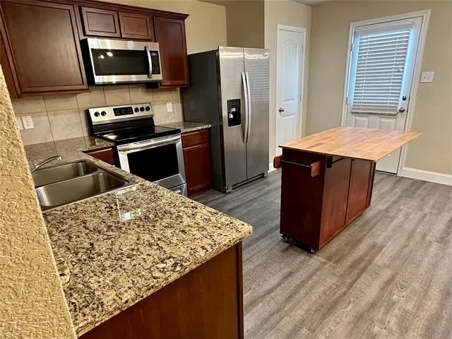 a kitchen with stainless steel appliances kitchen island granite countertop wooden cabinets a refrigerator a stove and a sink with wooden floor