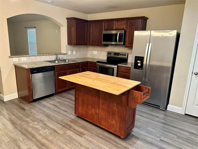 a kitchen with stainless steel appliances a sink a microwave a refrigerator and wooden floor