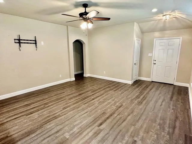 an empty room with wooden floor chandelier fan and windows