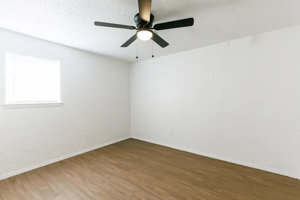 an empty room with wooden floor fan and windows