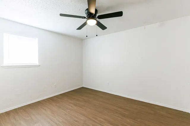an empty room with wooden floor fan and windows