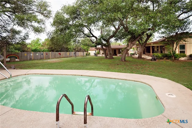 a view of a swimming pool with a yard and trees in the background