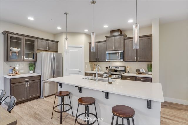 a kitchen with stainless steel appliances granite countertop a sink a stove a refrigerator island and chairs with wooden floor