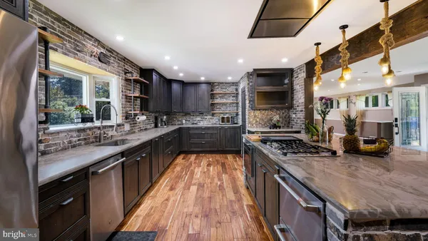 a kitchen with stainless steel appliances granite countertop a kitchen island a stove a refrigerator a sink a dining table and chairs with wooden floor