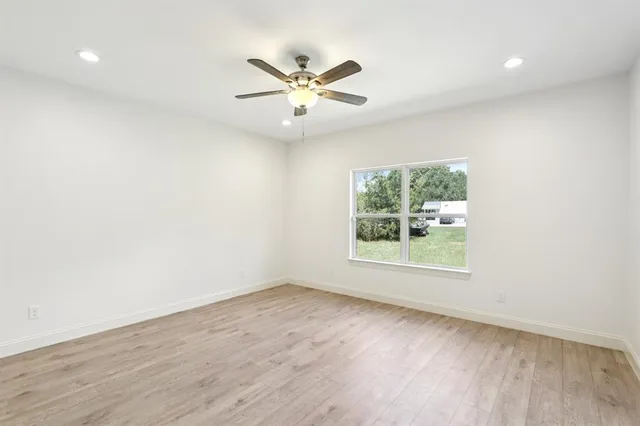 an empty room with wooden floor fan and windows