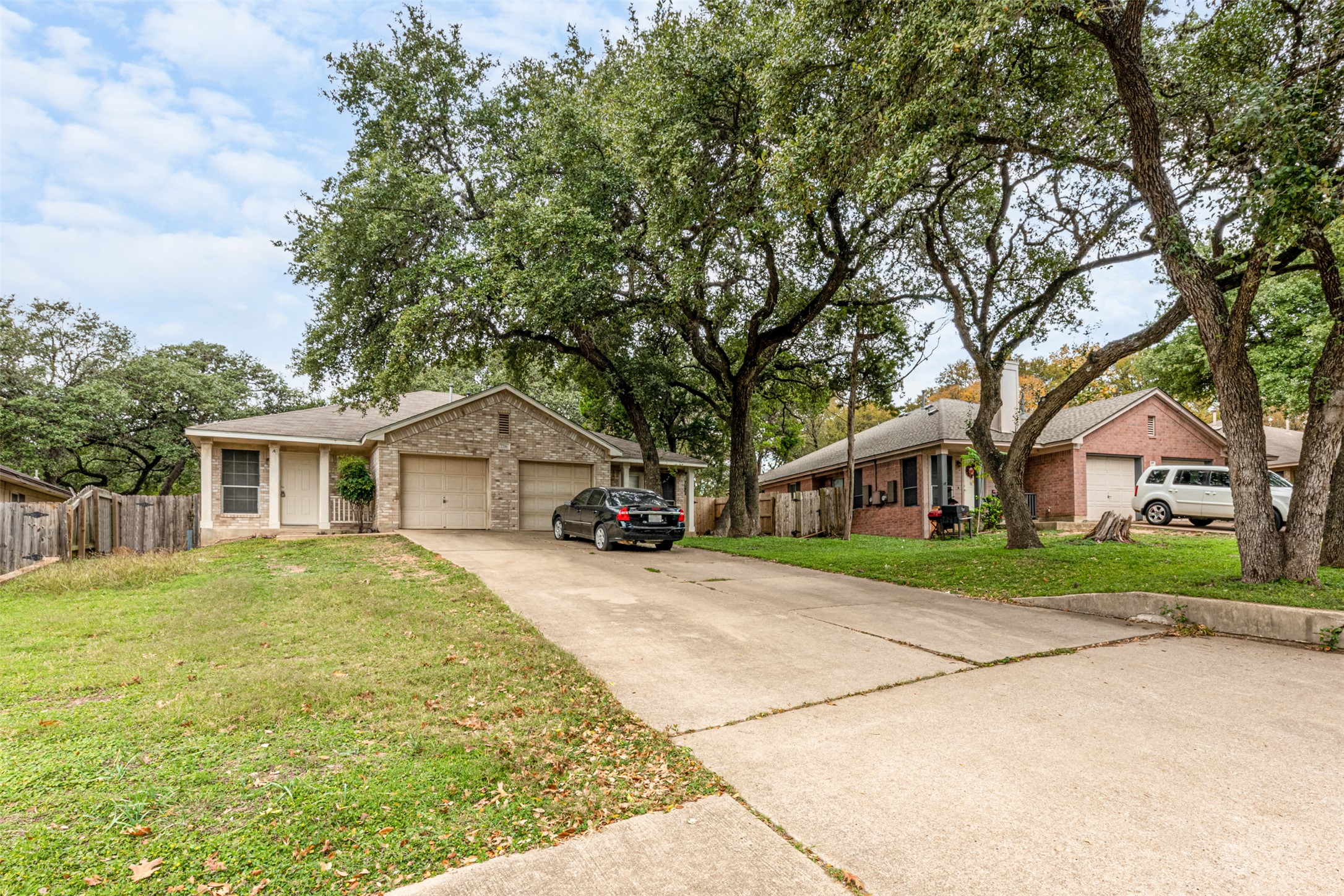Single-story brick exterior featuring a two-car garage, mature trees, and a concrete driveway