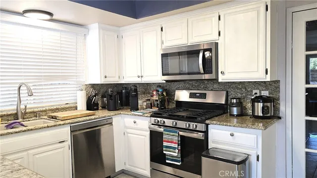 a kitchen with granite countertop white cabinets sink and stainless steel appliances