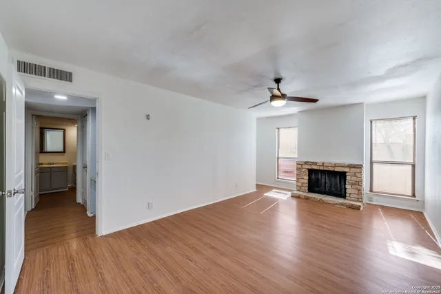 an empty room with wooden floor fireplace and windows